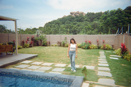 A woman stands in a manicured backyard with a pool.